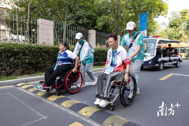 黄丽明（右）与自己的双打搭档吴桂妹在志愿者的协助下前往训练馆练球。