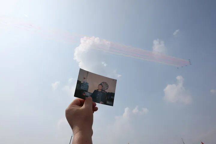 2025年9月3日，空中梯队飞过天安门广场时，王伟烈士的妻子阮国琴在观礼台上把王伟的照片举向蓝天。新华社记者 殷刚 摄