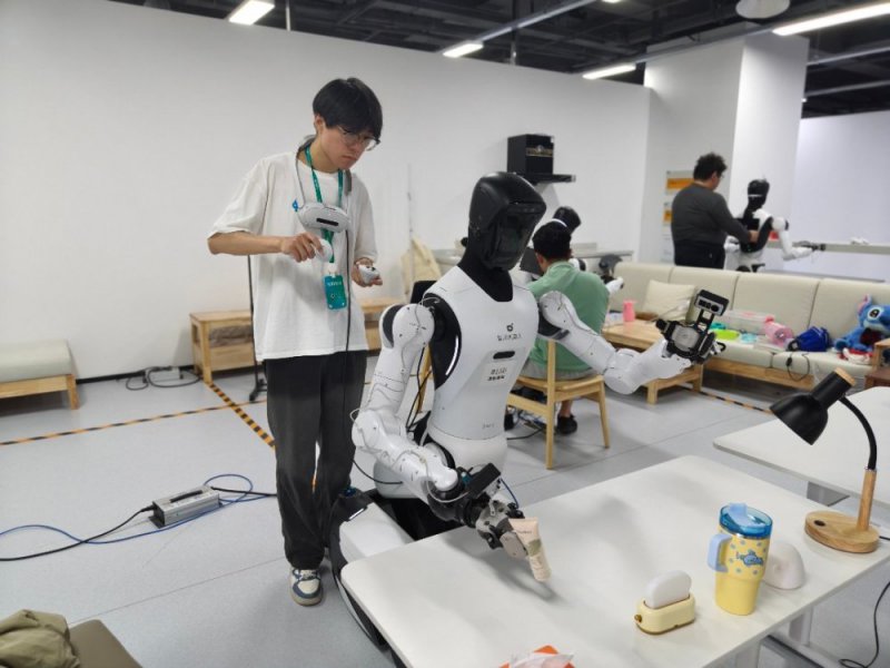 7月30日,浙江清华柔性电子技术研究院具身智能实训场里,一名00后数据采集员正在训练机器人拿取桌上的各种物件。中青报·中青网记者 宁迪/摄